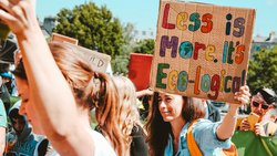 Das Bild zeigt eine Frau, die auf einer Kundgebung ein Plakat mit der Aufschrift "Less ist more -  It's ecological" hochhält.